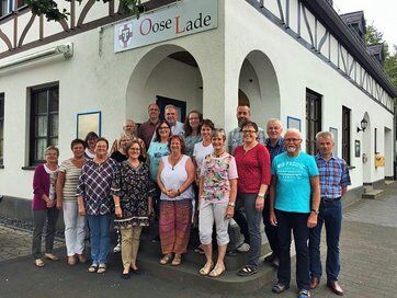 Gruppenbild mit Männer und Frauen vor einem Gebäude mit dem Schild "Oose Lade"
