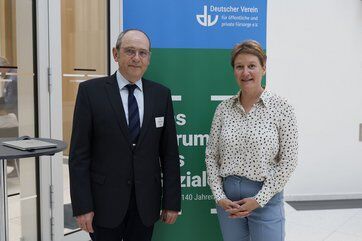 Bild mit Mann in Anzug und Kravatte und Frau in Bluse stehen vor einem Logo des Deutschen Vereins.