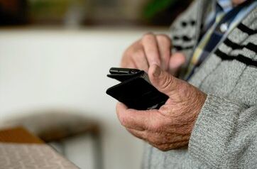 Bild von einer Nahaufnahme der Hände eines alten Mannes, der ein Mobiltelefon hält.