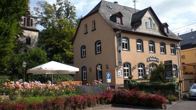 Bild mit altem schiefergedeckten Gebäude, davor ein Rosengarten mit Sonnenschirm