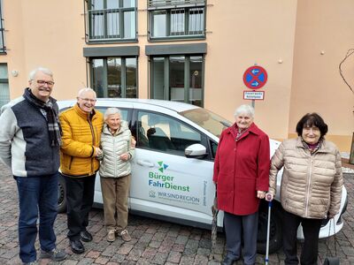 Bild mit einem Ehrenamtlichen Fahrer und drei Seniorinnen und einem Senior, die vor einem PKW stehen, mit dem Aufdruck Bürgerfahrdienst VG Linz