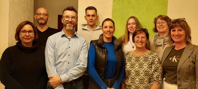 Gruppenfoto von 9 Personen, Männer und Frauen in zwei Reihen, die lachen.