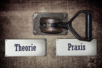 Bild mit zwei silbernen Plaketten, eines bedruckt mit Theorie und eines mit Praxis, darüber ein Hebel der, auf Praxis umgelegt ist.
