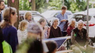 Menschen unterschiedlichen Alters sitzen lachend an einem Tisch am Straßenrand.