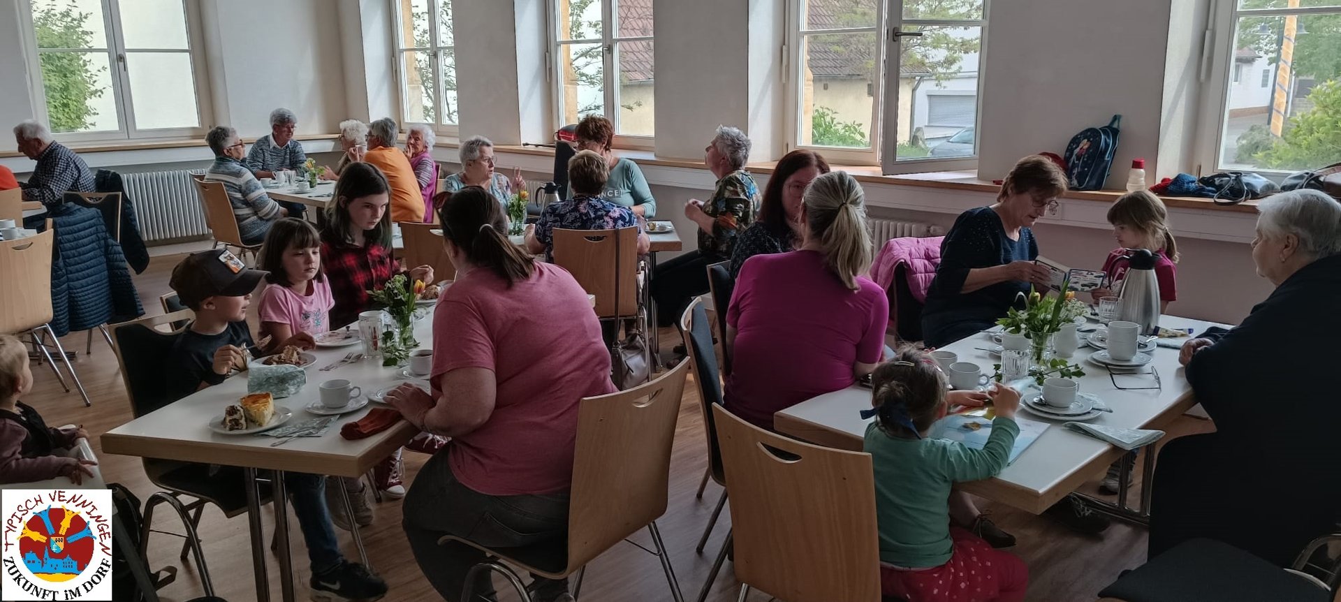 Menschen allen Alters sitzen an Tischen bei Kaffe und Kuchen