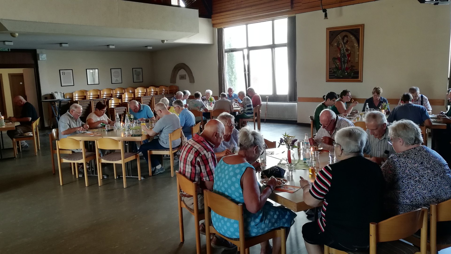 Vorwiegend ältere Männer und Frauen sitzen in Gruppen an Tischen und essen.