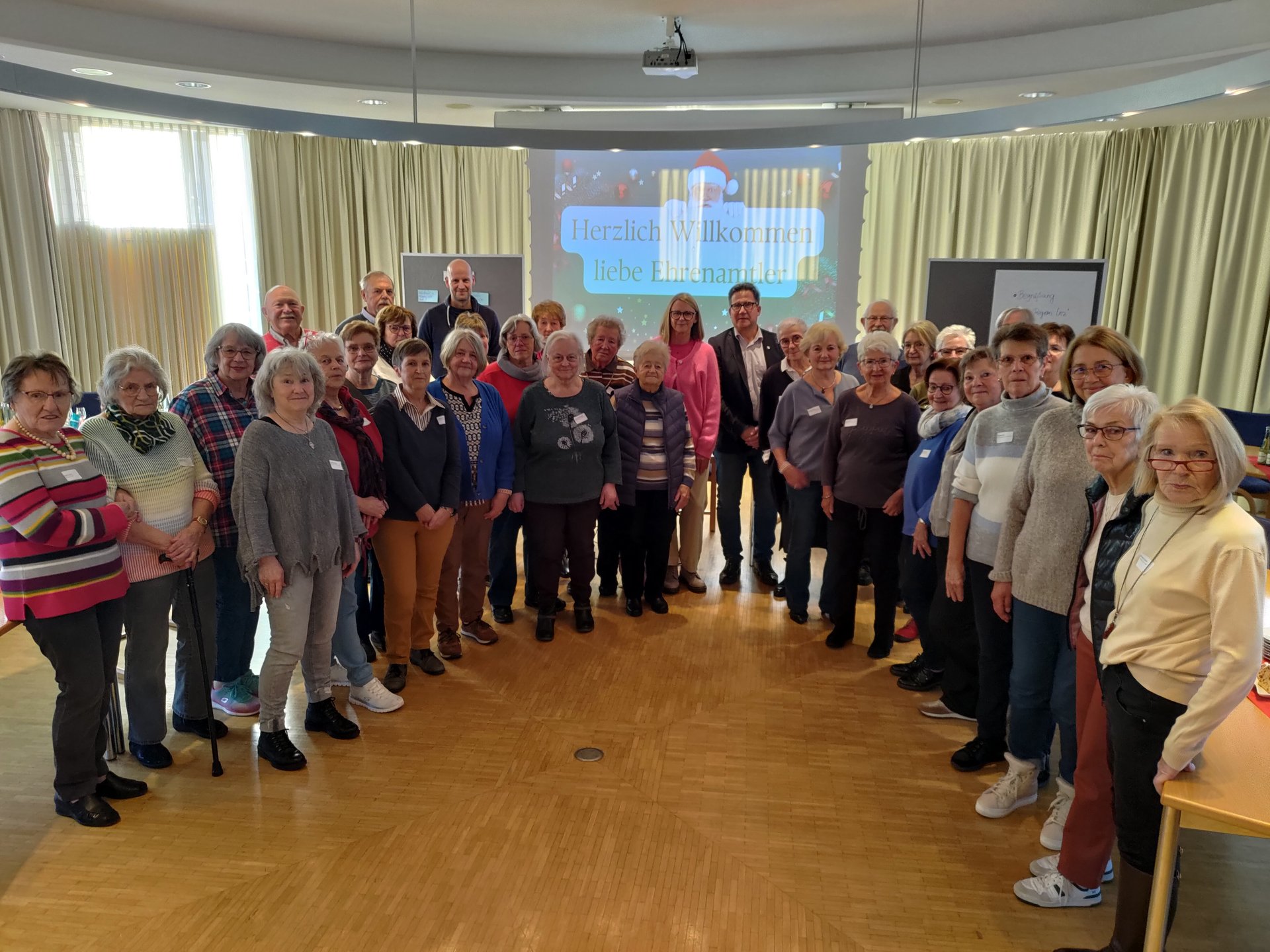 Gruppenbild mit vielen Männern und Frauen unterschiedlichen Alters, im Hintergrund eine Präsentation an der Wand.