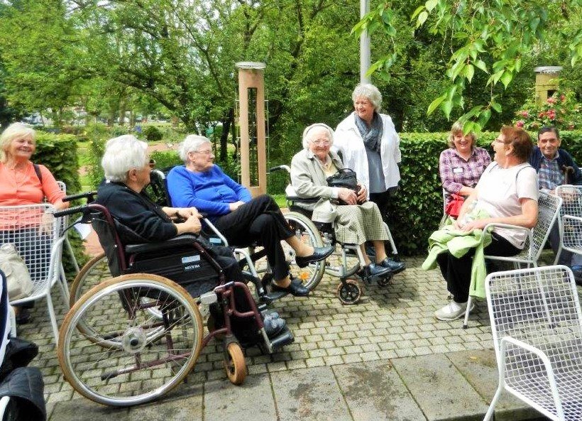 Zusammensitzen einer Gruppe von Menschen, zum Teil in Rollstühlen, auf einer Terasse