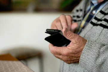 Bild von einer Nahaufnahme der Hände eines alten Mannes, der ein Mobiltelefon hält.