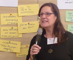 Uschi Rustler, Sprecherin der „Netten Nachbarn", mit Mikrofon vor einer Pinnwand auf einem Fachtag